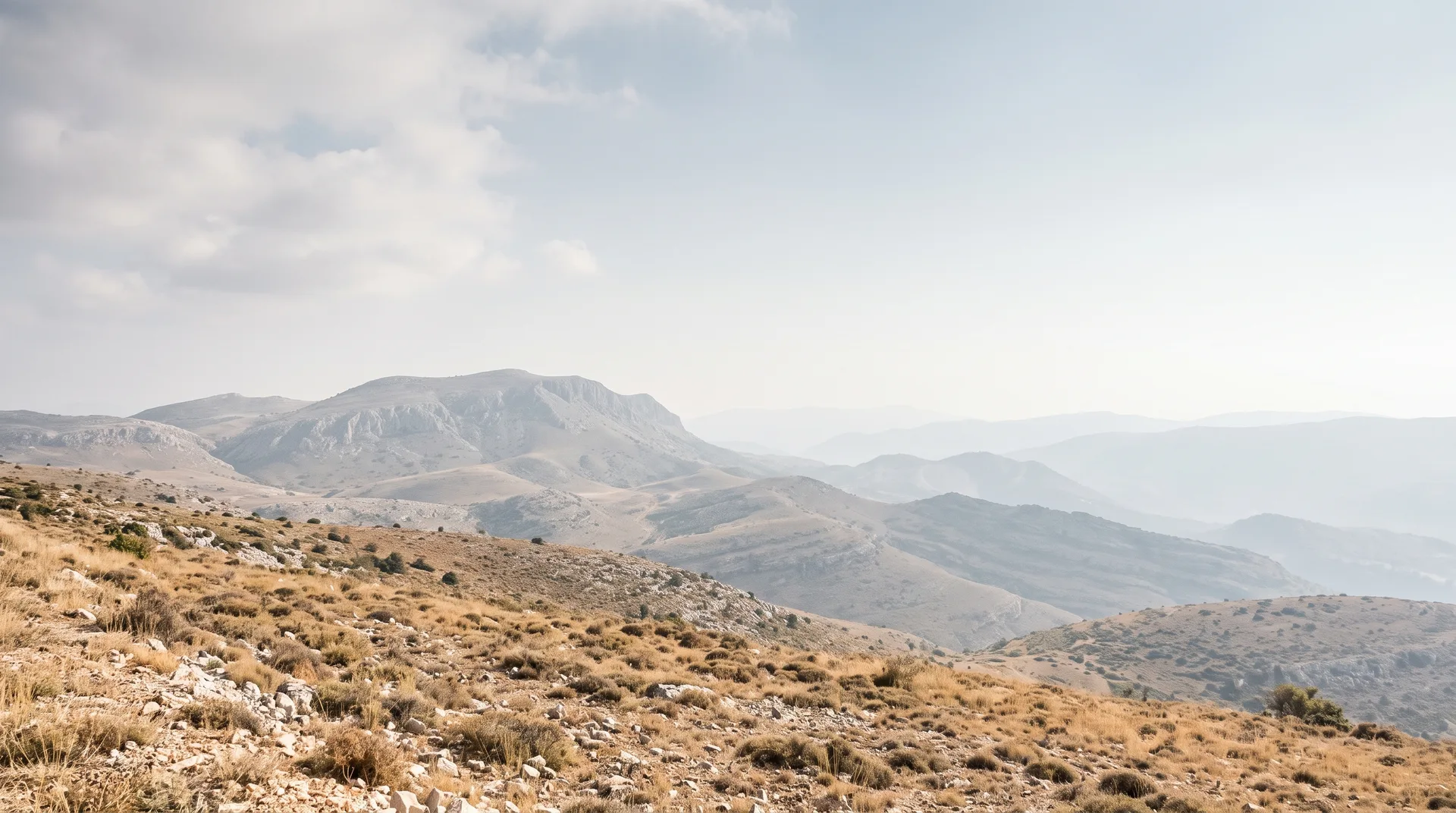 A wide upland of dry grass and pale limestone, ridges receding into haze under a bright overcast sky.