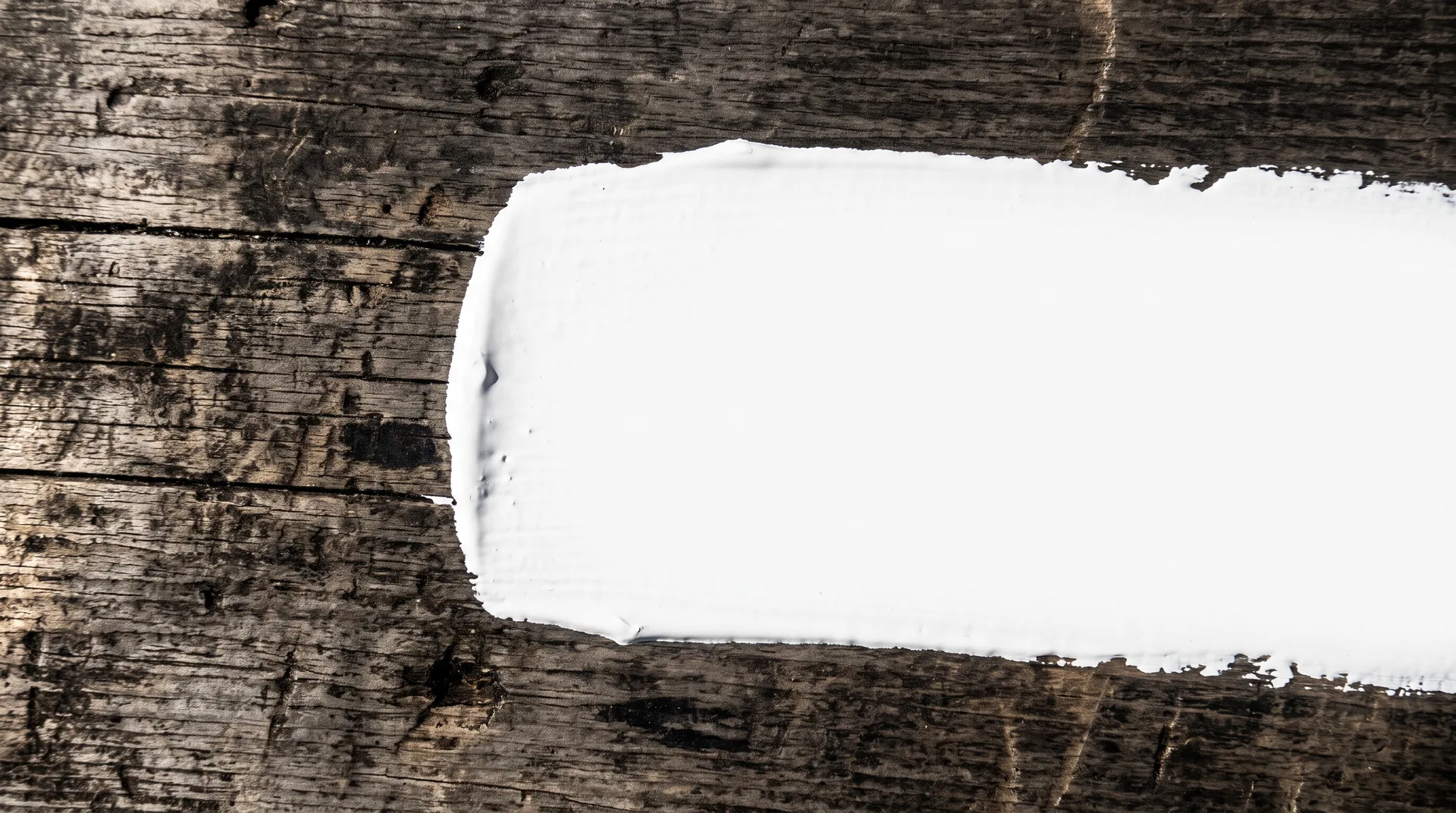 A broad stroke of thick white paint drawn across weathered grey-brown timber, hiding the grain beneath it completely.