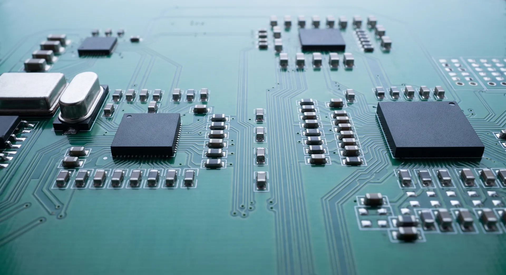 A dense green circuit board seen along its surface, hundreds of tiny rectangular components standing in rows between fine copper traces.