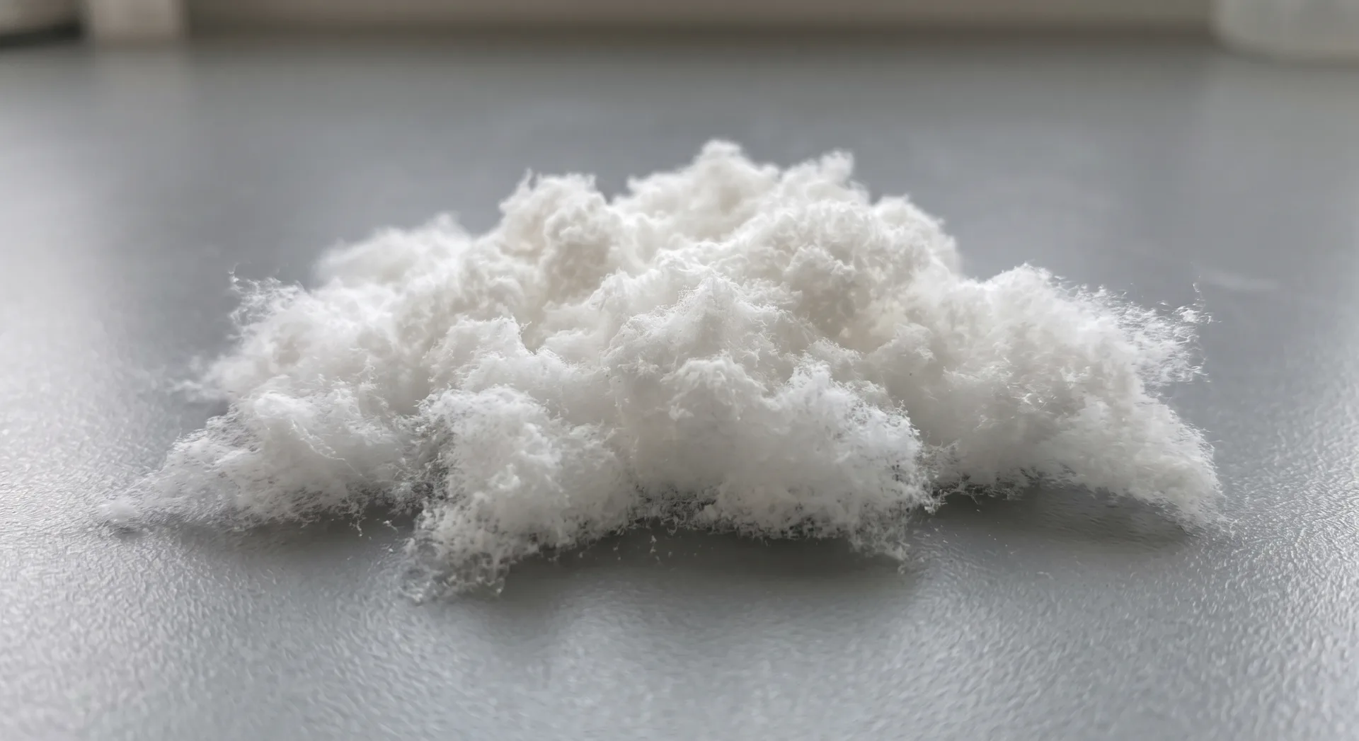A loose heaped mass of white powder resting directly on a grey surface, cottony and airy at the edges, looking almost weightless.